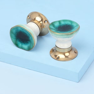 May include: Two ceramic door knobs with a green and white glaze. The knobs have a brass base and are designed with a circular shape.