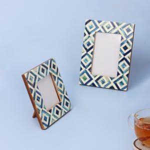 Pode incluir: Duas molduras decorativas com um padrão geométrico em tons de azul e branco. As molduras têm um fundo de madeira e um suporte. As molduras são exibidas em uma superfície azul clara.