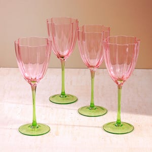 May include: Four pink wine glasses with a tulip-shaped design. The glasses have a green stem and base. The fluted design of the glass adds a decorative element. The glasses are suitable for serving wine or other beverages.