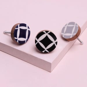 Op de afbeelding: Drie decoratieve kastknoppen met houten bases en patronen. Eén knop is marineblauw met een wit geometrisch ontwerp, een andere is zwart met een wit geometrisch ontwerp en de derde is grijs met een wit geometrisch ontwerp.