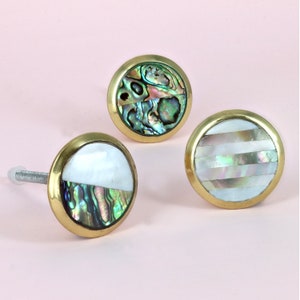 May include: Three round, gold-toned cabinet knobs with a white and iridescent mother-of-pearl inlay. The knobs have a polished finish.