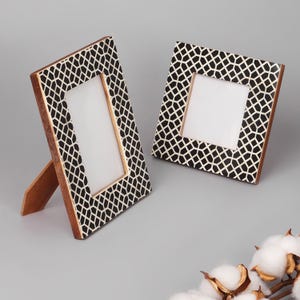 May include: Two decorative picture frames. The frames have a geometric black and white pattern on the front and a wooden stand on the back. The frames are square and rectangular, with a white space for a photo.