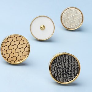 Könnte beinhalten: Vier dekorative runde Knöpfe mit goldener Einfassung. Die Knöpfe haben verschiedene Muster: Waben, weiß, kariert und Schlangenhaut.