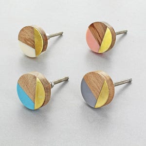 Può includere: Quattro pomelli decorativi per mobili dal design moderno. Ogni pomello presenta una base in legno, una sezione colorata e un accento in metallo dorato. I colori includono bianco, rosa, blu e grigio. Hanno una vite per l'installazione.