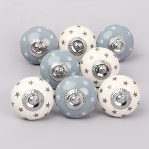 May include: Set of ten ceramic cabinet knobs with a star pattern. The knobs are half white with gray stars and half gray with white stars. The knobs have a silver finish.