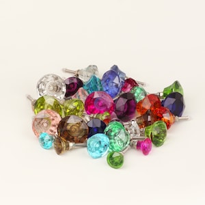 Peut inclure: Une collection de boutons de cabinet en verre coloré avec des bases en métal argenté. Les boutons sont de formes et de tailles variées, notamment rondes, ovales et carrées.