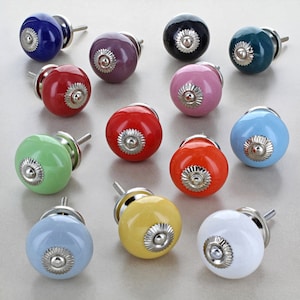 May include: Assortment of ceramic cabinet knobs in various colors, including blue, green, red, yellow, pink, and white. Each knob has a silver metal accent.