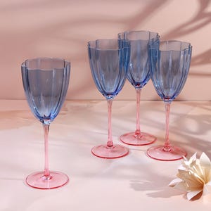 Op de afbeelding: Vier blauwe wijnglazen met roze stelen en voetjes staan op een lichtroze ondergrond. De glazen hebben een gegroefd ontwerp en een geschulpte rand. De stelen en voetjes zijn felroze.
