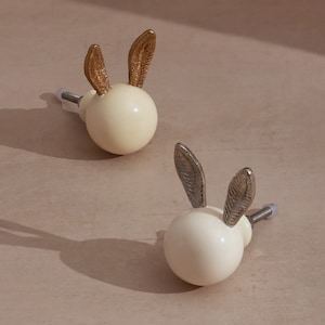 May include: Two white ceramic bunny door knobs with gold and silver bunny ears.