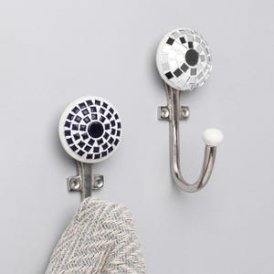 May include: Two decorative wall hooks with mosaic tile designs. One hook features a white and black mosaic, the other has a white and navy blue mosaic. Both have a silver-colored metal hook.
