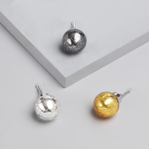 Pode incluir: Três puxadores decorativos para armários com efeito de vidro craquelado. Um é prateado, outro dourado e outro cinza escuro. Cada puxador tem um parafuso prateado para fácil instalação. Os puxadores são de formato esférico.