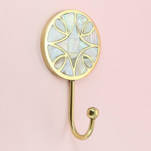Peut inclure: Un crochet mural doré avec un dessus rond décoratif en nacre blanche. Le crochet est en forme de crochet simple et incurvé.