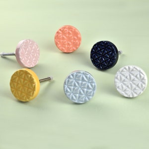 May include: Six ceramic cabinet knobs with a geometric pattern. The knobs are in various colours, including pink, yellow, blue, white, and light blue.