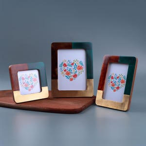 May include: Three decorative picture frames with a heart-shaped floral design. The frames have a mix of brown, green, and gold accents. The frames are displayed on a wooden surface.
