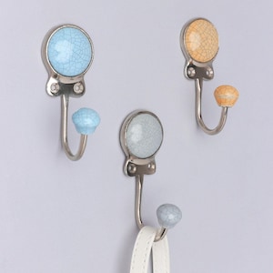 May include: Three ceramic hooks with a crackled glaze finish. The hooks are in blue, light blue, and yellow. The hooks are mounted on a light gray wall.