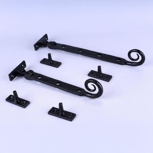 May include: Black wrought iron window hardware set. The set includes two long, rectangular latches with a decorative scroll design at one end, and several smaller rectangular pieces with a central peg. The hardware is designed for window or door use.