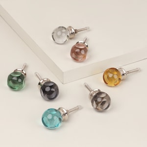 Pode incluir: Conjunto de 10 botões de armário de vidro com bases de metal prateado. Os botões são de várias cores, incluindo transparente, verde, azul, cinza e marrom.