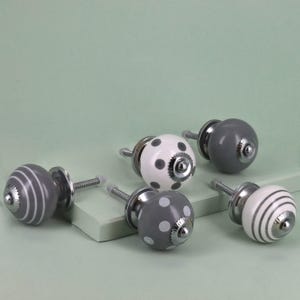 May include: A selection of decorative cabinet knobs in various designs. The knobs are in shades of grey and white, with polka dot and striped patterns. Each knob has a silver-coloured base and screw.