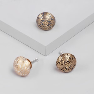 May include: Three decorative cabinet knobs with a floral pattern. The knobs are in gold, white, and black.