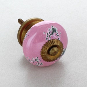Könnte beinhalten: Rosafarbener Keramik-Schrankknopf mit goldfarbenem Metallakzent und schwarzen Flecken.