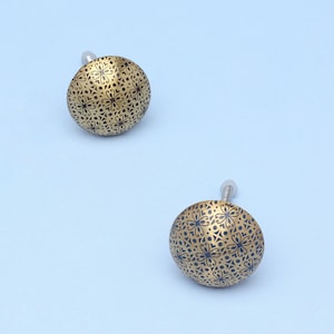 Può includere: Due pomelli decorativi color oro con intricati motivi floreali neri. Ogni pomello ha una forma arrotondata e una vite argentata per il fissaggio. I pomelli sono su uno sfondo azzurro.