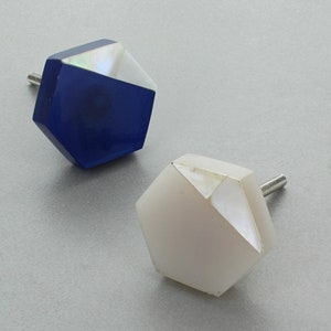 Op de afbeelding: Twee zeshoekige kastknoppen met een witte en blauwe iriserende afwerking. De knoppen hebben een zilveren schroef.