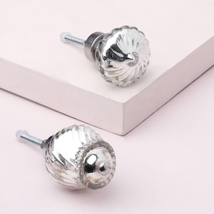 Peut inclure: Deux boutons de meuble en verre transparent avec un motif en spirale et une quincaillerie en métal argenté. Les boutons sont sur une surface blanche, offrant une touche décorative pour les meubles. Les boutons mesurent environ 3,8 cm de diamètre.