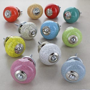 May include: A selection of colourful ceramic cabinet knobs. The knobs are round with a crackle glaze finish and silver-toned metal hardware. Colours include red, yellow, green, blue, pink, and white.