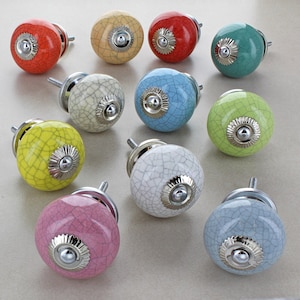 Puede incluir: Surtido de 10 pomos de armario de cerámica con acabado craquelado y detalles plateados. Los pomos son de varios colores, incluyendo amarillo, azul, verde, rosa, rojo y crema.