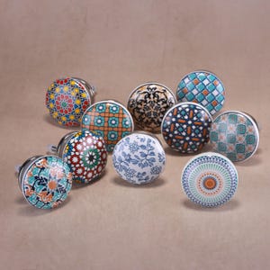 May include: A collection of decorative ceramic cabinet knobs with various colorful geometric and floral patterns. Each knob has a silver-toned metal base. The knobs feature designs in shades of blue, orange, red, green, and black.