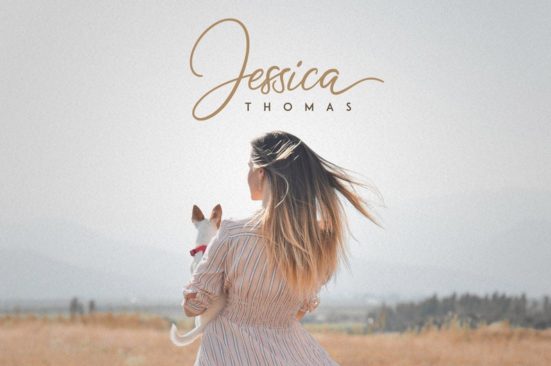 May include: A woman with long blonde hair is holding a small white dog in her arms. She is wearing a striped pink and white dress. The background is a field of dry grass.