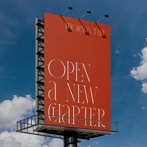 May include: A large billboard against a blue sky with white clouds. The billboard is a vibrant orange-red color and features the text "THORN & TALE" at the top and "OPEN a NEW CHAPTER" in elegant white lettering. The structure has a metal frame.