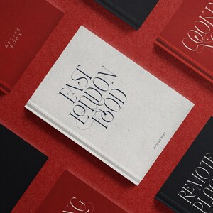 May include: A collection of hardcover books with titles including "East London Food," "Cooking Notes," and "Remote Places." The books are in red, black, and white, arranged on a red surface. The titles are in elegant, stylized fonts.
