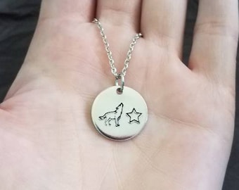 May include: A silver necklace with a round pendant featuring a wolf howling at a star. The pendant is on a silver chain.