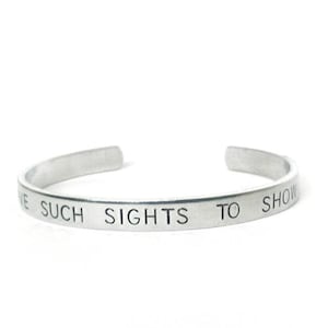 May include: A silver-colored cuff bracelet with the engraved text "WE SUCH SIGHTS TO SHOW". The open-ended bracelet is made of a shiny, metallic material and is displayed against a white background.