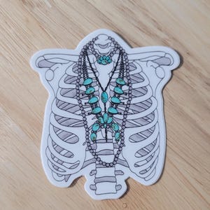 May include: A white sticker with a line drawing of a ribcage with a turquoise and silver necklace inside.