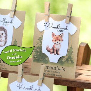 Puede incluir: Un sobre de semillas de papel marr&oacute;n con un recorte blanco en forma de body, una ilustraci&oacute;n de un zorro y el texto Woodland BABY. El sobre se sujeta con una pinza de madera y muestra el texto Samantha's BABY SHOWER WILDFLOWER SEEDS.