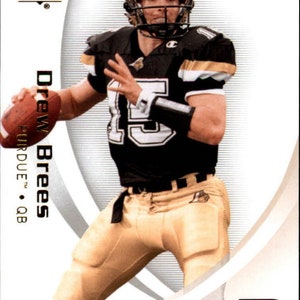 May include: A white and gold football card featuring Drew Brees, a quarterback for Purdue University. The card has a white background with a gold border and a gold "SP Authentic" logo in the top left corner. The card also features a gold "P" logo in the bottom right corner. The card is numbered "15" in the bottom left corner.