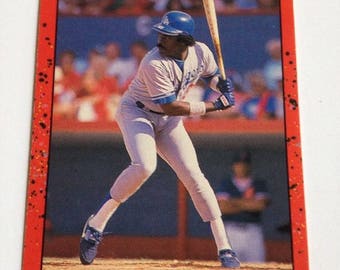 May include: A baseball card featuring a baseball player in a blue and white uniform, swinging a bat. The card is red with black and white speckles. The card reads "Donruss 90 Eddie Murray 1B Dodgers".