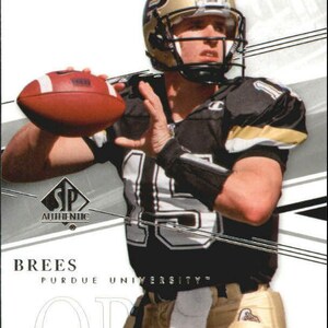 Puede incluir: Una camiseta de fútbol negra y dorada con el número 15 en la parte delantera. La camiseta tiene el texto "Purdue University" en la parte delantera. Un jugador de fútbol que lleva la camiseta está sosteniendo un balón de fútbol marrón. El jugador lleva un casco dorado con una máscara facial negra. El fondo es blanco con líneas negras y plateadas.