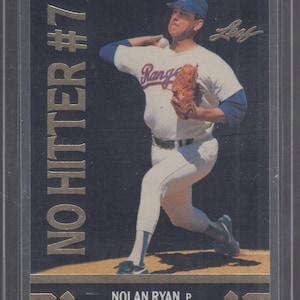 May include: A baseball card featuring Nolan Ryan, a pitcher for the Texas Rangers. The card is black with gold accents and the text "NO HITTER #7" in gold. Ryan is wearing a white and blue Rangers uniform and is in a pitching stance. The card is signed "Ryan" in gold.