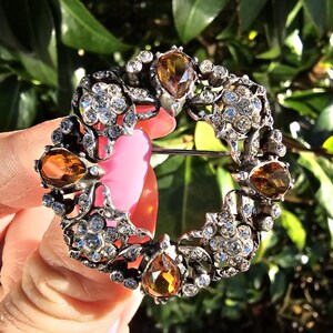 Puede incluir: Un broche de plata con un diseño circular que presenta un delicado patrón floral y cuatro piedras de ámbar en forma de pera.