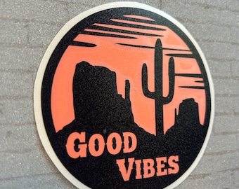 May include: A black and orange round sticker with a silhouette of a desert landscape, a cactus, and the text "GOOD VIBES".
