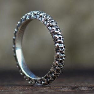May include: A silver ring with a textured, patterned design. The ring is thin and delicate.