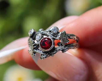 May include: A silver ring with a red gemstone and small white gemstones set in a branch-like design.