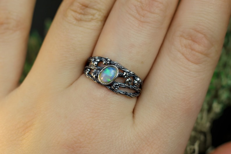 May include: A silver ring with a delicate, intricate design featuring a branch-like pattern and a white opal gemstone.