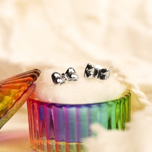 May include: A pair of silver bow-shaped earrings in a colorful glass jewelry box with a white cotton lining.