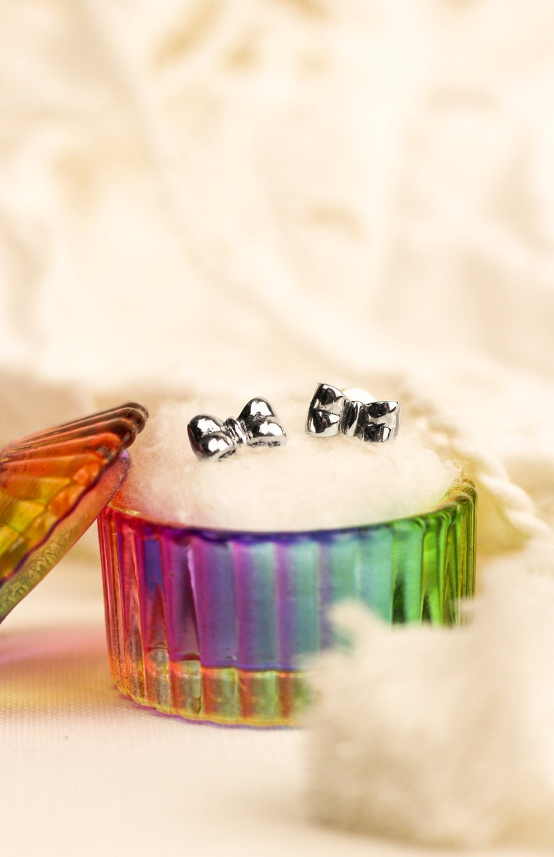 May include: A pair of silver bow-shaped earrings in a colorful glass jewelry box with a white cotton lining.