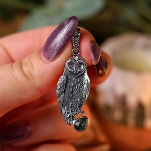 May include: A detailed silver owl pendant with a dark patina, featuring intricate feather detailing and a small green gemstone. The owl is suspended from a delicate chain, showcasing a gothic or fantasy theme.
