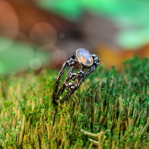 May include: A silver ring with a delicate floral design and a white opal gemstone. The ring is set on a bed of green moss.